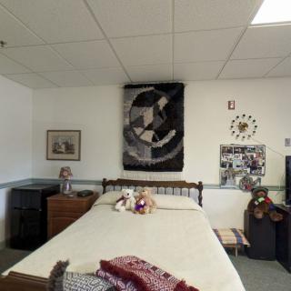 A cozy bedroom with a neatly made bed, decorated with a geometric poster and stuffed animals.