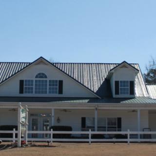 A two-story house with a metal roof and a front porch, surrounded by a white fence.