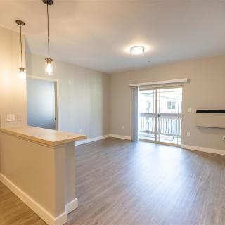 An empty living room with wood flooring and pendant lights, featuring a sliding glass door leading to a balcony.