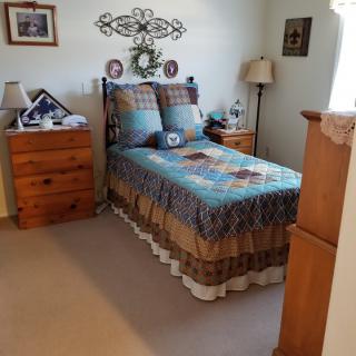 A cozy bedroom with a neatly made bed, adorned with a patchwork quilt. Wooden nightstands flank the bed, topped with lamps and decor. Wall art adds a personal touch to the room.
