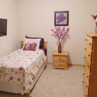 A cozy bedroom with a single bed adorned with floral bedding, matching wall art, and wooden furniture.