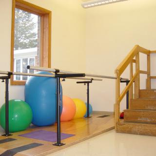 A well-equipped therapy room featuring balance bars, a staircase, and colorful exercise balls.