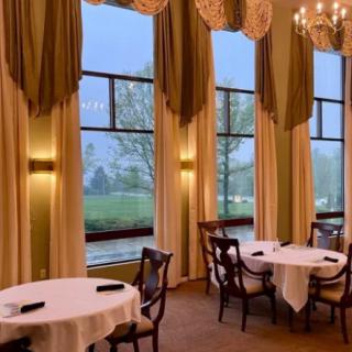 An elegant dining room with round tables, large windows, and chandeliers.