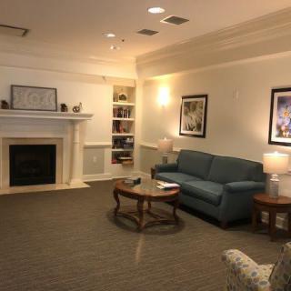 A cozy living room with a couch, coffee table, and fireplace, adorned with artwork and a bookshelf.