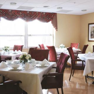 An elegantly set dining area with neatly arranged tables and chairs, featuring white tablecloths and floral centerpieces.