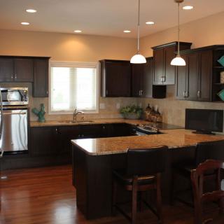 A modern kitchen with dark cabinets and a central island, illuminated by pendant lights.