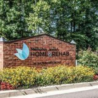 Sign for a home rehab center on a brick wall surrounded by trees and landscaped plants.
