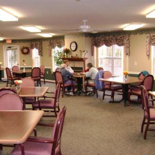 A communal dining area with tables and chairs where people are gathered for a meeting.