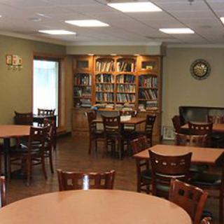 A cozy library interior with tables and chairs, surrounded by bookshelves.