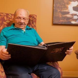An elderly man sitting in a chair, reading a book indoors.