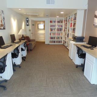 A modern office space featuring multiple computers, workstations, and bookshelves.