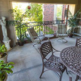 A cozy balcony adorned with patio furniture, lush plants, and a decorative statue.
