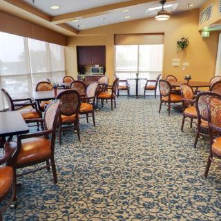 A spacious and elegantly decorated dining area featuring multiple tables and chairs, with carpeted flooring and large windows allowing natural light.