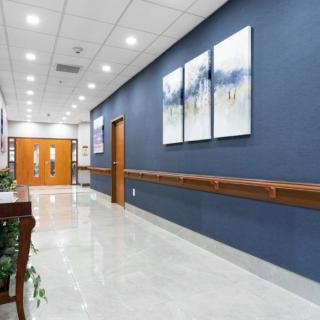 A well-lit hospital hallway with artwork on the walls and double doors at the end.