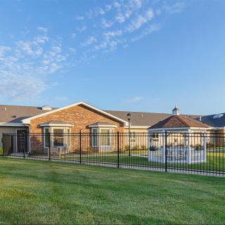 A single-story brick house with a fenced yard and a gazebo under a clear sky.