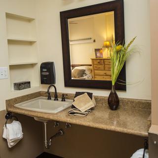 A bathroom counter with a sink, mirror, and decorative vase with flowers.