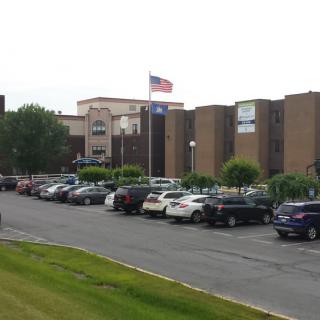 A parking lot filled with cars in front of a building with flags on display.