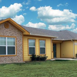 A suburban house with brick and yellow siding under a cloudy sky.