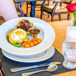 A delicious brunch plate featuring a fried egg, potatoes, mini pancakes, and syrup served at a restaurant table.