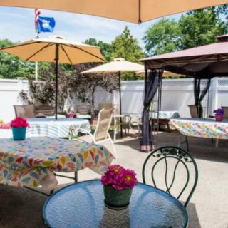A cozy outdoor patio area featuring tables with umbrellas, colorful flowers, and a gazebo.