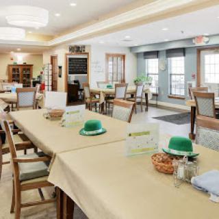 A spacious dining area set up for a communal meal, featuring tables adorned with green hats and a warm, inviting interior.