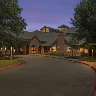 A nighttime view of a building with a well-lit exterior, surrounded by trees and a circular driveway.