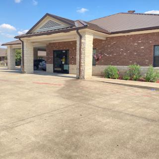 A view of a modern commercial building with a parking lot and landscaped areas under a clear blue sky.