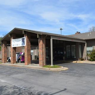 A small brick car wash with a banner displayed above the entrance on a sunny day.