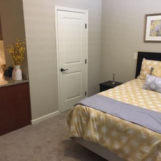 A cozy bedroom featuring a bed with patterned bedding, a nightstand, and a closed door.