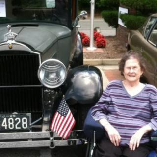 A woman sitting in front of a vintage car adorned with an American flag.