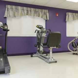 A gym room with exercise equipment including a treadmill and stationary bike against purple walls.