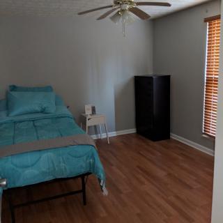 A simple bedroom with a single bed, ceiling fan, and wooden floors.
