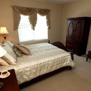 A cozy bedroom featuring a large bed with decorative pillows, an elegant armoire, and soft lighting from a bedside lamp.
