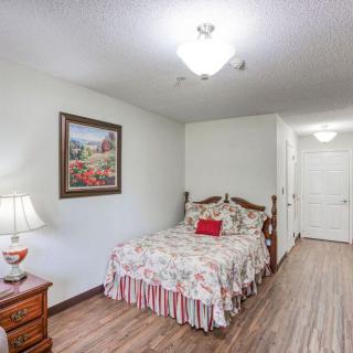 A cozy bedroom with floral bedding, a bedside table with a lamp, and a framed painting on the wall.