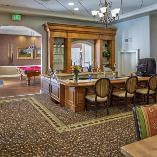 A cozy interior featuring a wooden bar with seating, a billiard table, and elegant lighting.