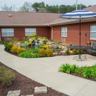 A beautifully landscaped outdoor area featuring a winding pathway, vibrant flowers, and a shaded seating area with an umbrella.