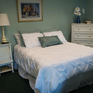 A cozy bedroom with a neatly made bed, a nightstand with a lamp, and a dresser against the wall.