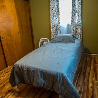 A cozy bedroom with a single bed, wooden floor, and patterned curtains.