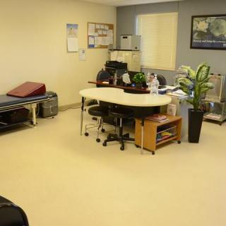 A tidy medical office with a desk, chairs, and a treatment table.