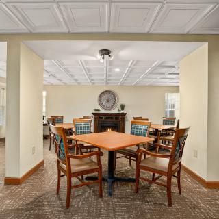 A cozy dining area with wooden tables and chairs, featuring a carpeted floor and ceiling light fixtures.