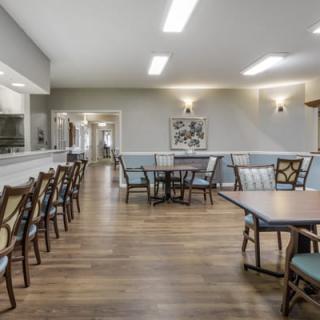 A well-lit dining area with wooden floors, containing several tables and chairs.
