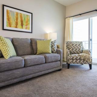 A cozy living room with a gray sofa and an armchair, decorated with yellow and green pillows, featuring artwork on the wall.
