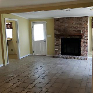 An empty living room with a brick fireplace and tiled floor.