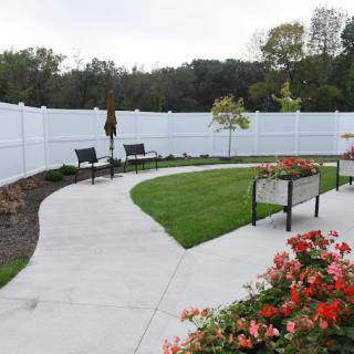 A landscaped garden with a winding pathway, benches, and vibrant flowers along a white fence.