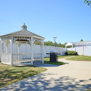A serene gazebo in a sunny park, surrounded by a walking path and lush greenery.