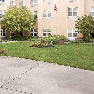 A well-maintained garden in front of a multi-story building with a lawn, trees, and an American flag.
