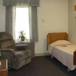 A cozy bedroom with a single bed, armchair, and window with curtains.