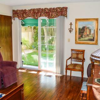 A cozy living room with a plush armchair, wooden floors, and natural light streaming through a sliding glass door.