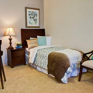 A neatly arranged bedroom with a single bed, nightstand, lamp, and chair.