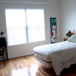 A minimalist bedroom featuring a bed, desk, and large window with wooden flooring.